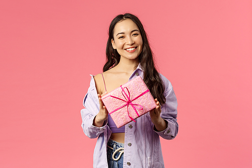 Girl have a present for you. Portrait of stylish pretty young asian female holding wrapped gift box and smiling at camera as being invited to birthday party, standing pink background.