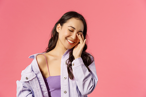 Lifestyle, people and emotions concept. Close-up portrait of cheerful attractive, stylish korean girl laughing, touching eye and smiling with closed eyes, having funny conversation, pink background.