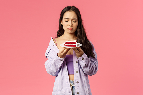 Portrait of gloomy upset asian female sighing, look uneasy and distressed at delicious piece cake but cant eat it, express regret and disappointment, standing pink background distressed.