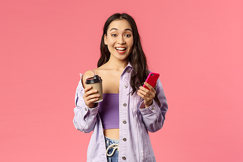 Portrait of surprised attractive, smiling woman holding smartphone and take-away coffee seeing friend on street and being excited meeting her, standing pink background enthusiastic.
