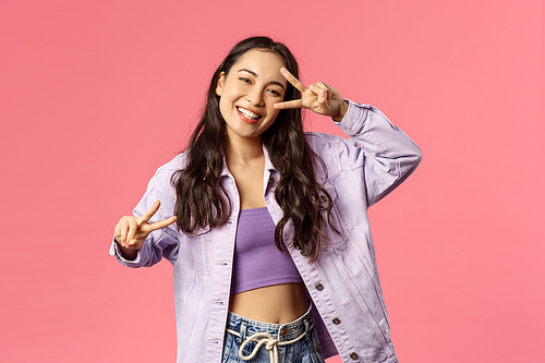 Portrait of charismatic good-looking asian girl sending positive vibes, show peace kawaii gesture near face and dancing, smiling inviting people to visit her store or apply company, pink background.