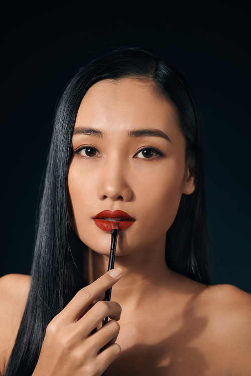 Young charming woman applying lipstick against black background.