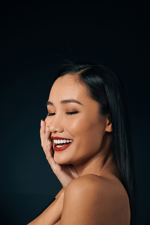 Beautiful young woman in lace top with red lips touching face. Over black background. Copy space.