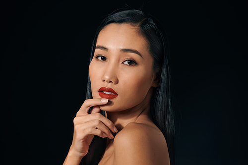 Beautiful young woman in lace top with red lips touching face. Over black background. Copy space.