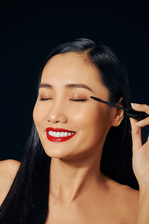 Close-up portrait of nice lovely cute sweet attractive cheerful positive Asian woman holding in hands applying trendy black mascara isolated