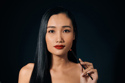 Asian woman holding lipstick over balck background