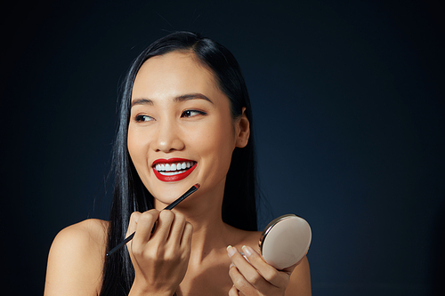 Makeup artist applies red lipstick. Beautiful female face. Hand of a make-up master painting lips of a young girl beauty model. Makeup in progress