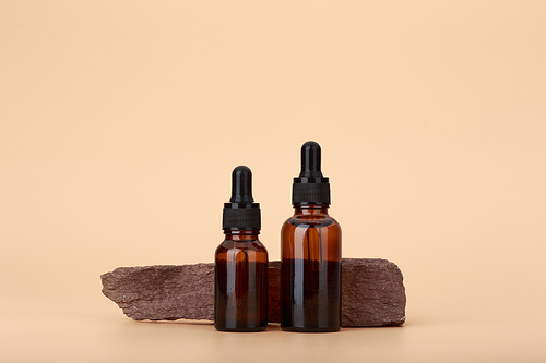 Two skin serum bottles next to natural stone against beige background with copy space. Concept of luxury skin serum or oils for anti aging treatment or daily nourishing and moisturizing treatment