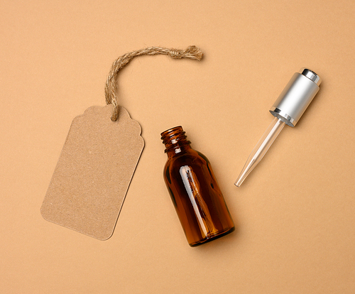 paper tag and glass cosmetic brown bottle with a pipette on a beige background. Cosmetics SPA branding mockup, top view
