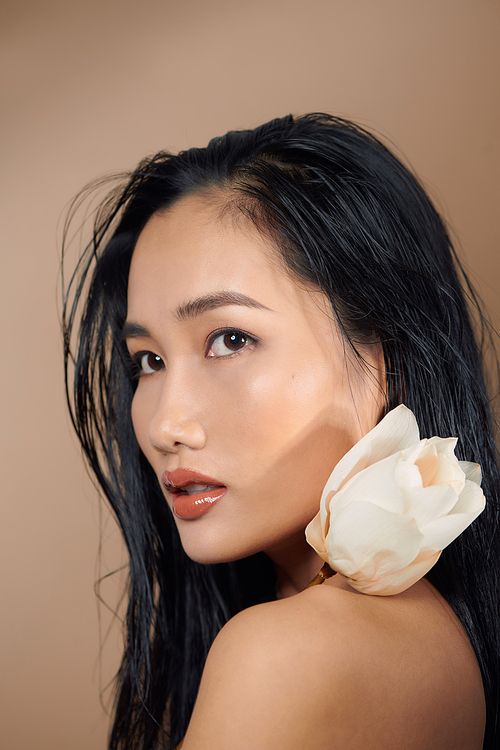 Attractive long-haired girl smiling and holding dried lotus buds on beige background.