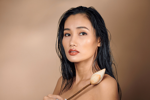 A young beautiful tan skin Asian girl holding dried lotus buds on beige background.