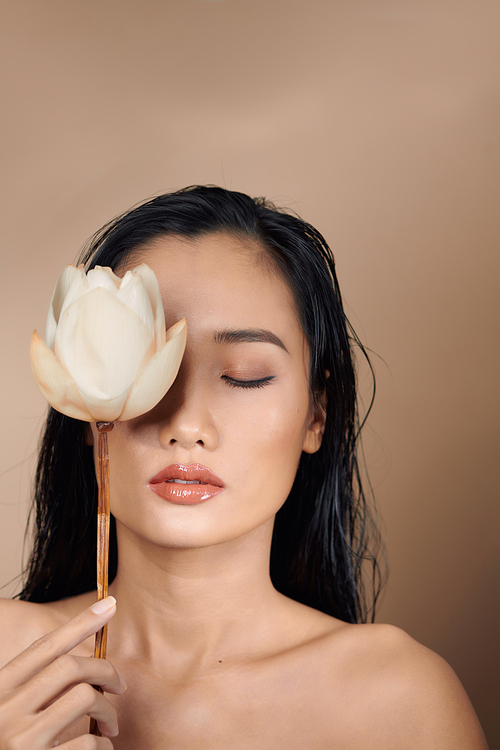 Attractive sensual woman holding dried lotus buds isolated on beige background.