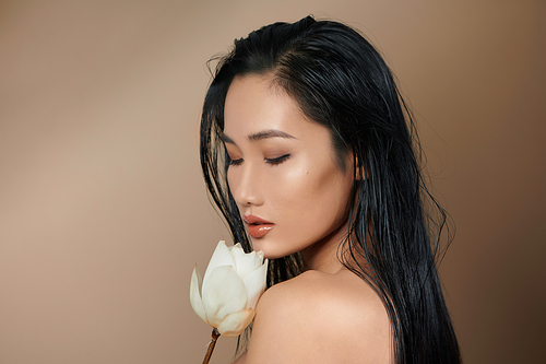 Woman got dark tan skin with long hair and holding flowers on beige background in white cropped top