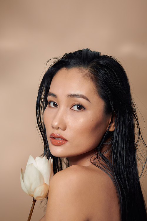 Young healthy Asian woman portrait holding dried lotus buds on beige background.