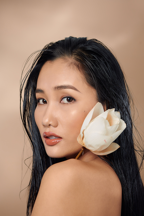 Attractive sensual woman holding dried lotus buds isolated on beige background.