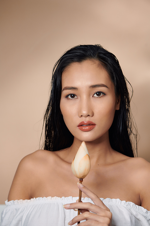 Fresh, natural skin. Attractive sensual woman with tan skin, holding dried lotus buds isolated on beige background