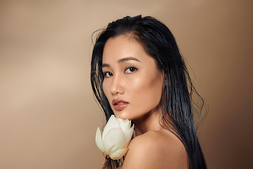 A young beautiful tan skin Asian girl holding dried lotus buds on beige background.