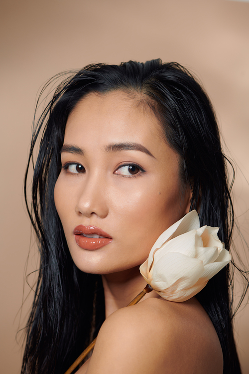 Fresh, natural skin. Attractive sensual woman with tan skin, holding dried lotus buds isolated on beige background