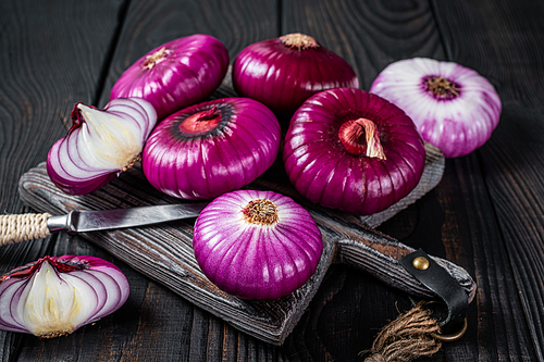 Whole and halfed Flat red sweet onion on a cutting board. Black Wooden background. Top View.