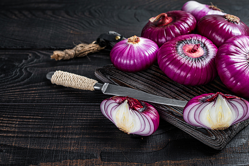 Whole and halfed Flat red sweet onion on a cutting board. Black Wooden background. Top View. Copy space.