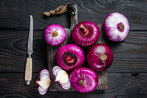 Whole and halfed Flat red sweet onion on a cutting board. Black Wooden background. Top View.