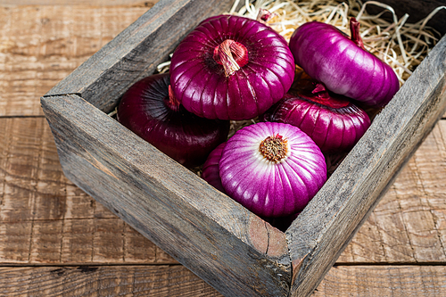 Flat red sweet onion in wooden box. Wooden background. Top View.