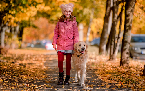 Preteen girl kid with golden retriever dog standing at autumn park and looking at camera. Beautiful portrait of child and pet doggy outdoors at nature