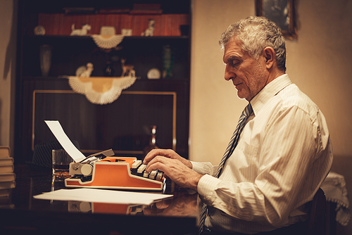 Retro senior man writer typing on obsolete typewriter.