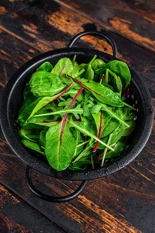 Fresh raw mixed greens, spinach, swiss chard and arugula. Dark wooden background. Top view.