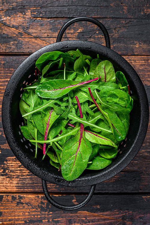 Fresh raw mixed greens, spinach, swiss chard and arugula. Dark wooden background. Top view.