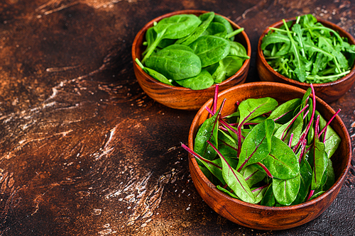 Mix Salad leafs, Arugula, Spinach and swiis Chard in wooden bowls. Dark background. Top view. Copy space.