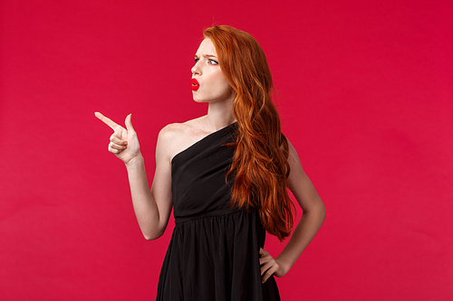 Portrait of suspicious or uncertain young confused redhead woman asking question about strange thing, pointing and looking upper left corner squinting puzzled, hard to see what there.