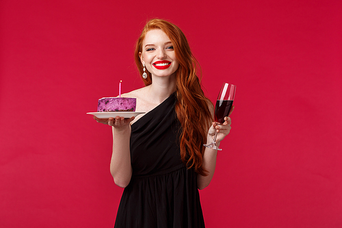 Waist-up portrait of gorgeous feminine young redhead woman celebrating birthday, drinking glass of wine and hold cake with lit candle smiling as making wish blow out for dream come true.