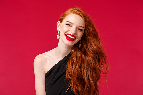 Makeup, beauty and women concept. Close-up portrait of gorgeous and stylish young redhead feminine woman standing over red background with lipstick, laughing, ginger hair flying in air.