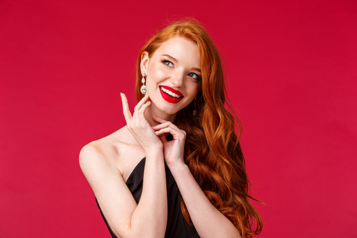 Beauty, fashion and luxury concept. Close-up portrait of gorgeous feminine redhead woman in red lipstick and black dress, touching earring look away with dreamy happy smile.