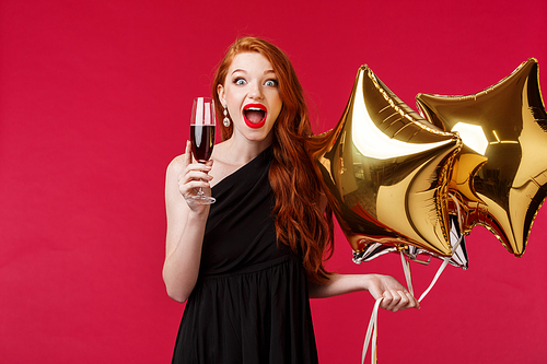 Portrait of excited gorgeous and wondered, surprised redhead woman celebrating birthday or having party with friends, raising glass of champagne or wine, gasping happy hold balloons.