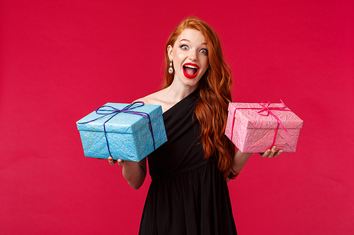 Celebration, holidays and women concept. Portrait of excited and happy feminine redhead woman in black stylish dress, holding two birthday gifts, blue and pink boxes, smiling amazed and cheerful.