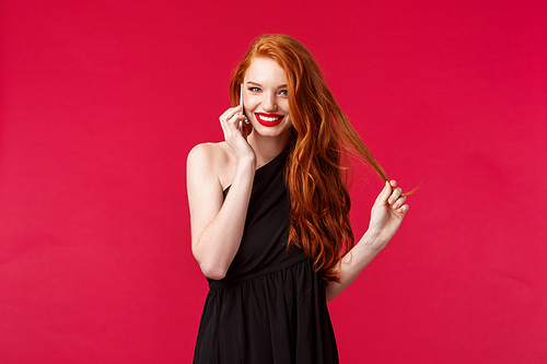 Portrait of coquettish flirty feminine redhead woman in black dress giggle while talking on phone with bae, hold smartphone near ear calling someone flirting and smiling, wear black dress.