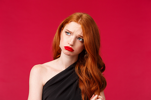 Close-up portrait of silly upset and gloomy young woman with red curly hair, grieving feel uneasy, sighing and grimacing concerned look away, standing in black dress, being left at party alone.