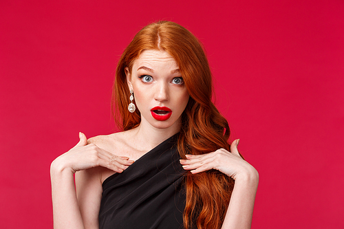 Close-up portrait of shocked gorgeous redhead woman look with disbelief and shook, questioned pointing at herself, being accused or blamed in something, stand in black dress red background.