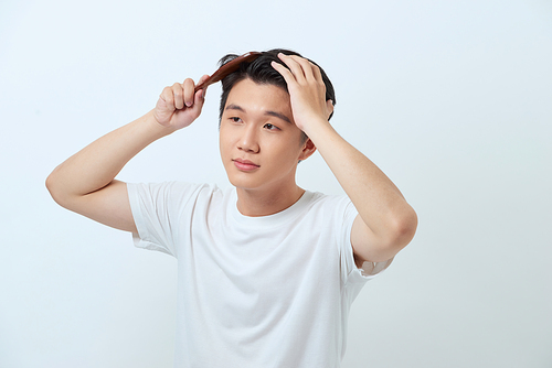 Smiling young man brushing hair with comb on white background