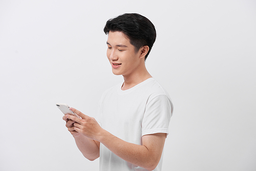 Handsome smiling man in white t-shirt holding smartphone and typing sms.