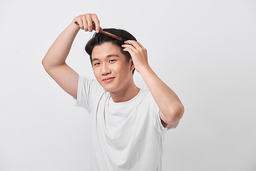 people concept - smiling young man brushing hair with comb on white background