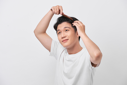 beauty, grooming and people concept - smiling young man brushing hair with comb over white background