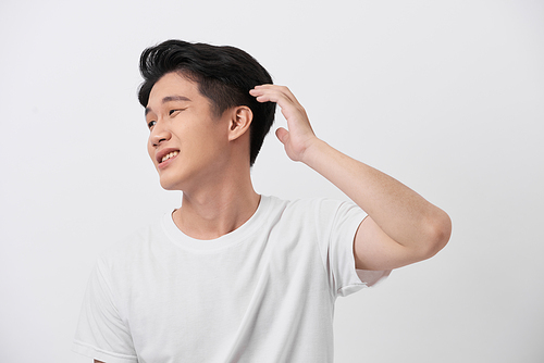 Confident smiling handsome young man in white t shirt. standing on the pure background, fixing his perfect hairstyle