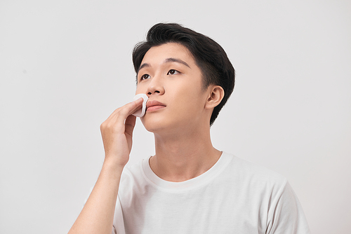 Beauty portrait of confident young man using cotton pad on his face isolated over white background