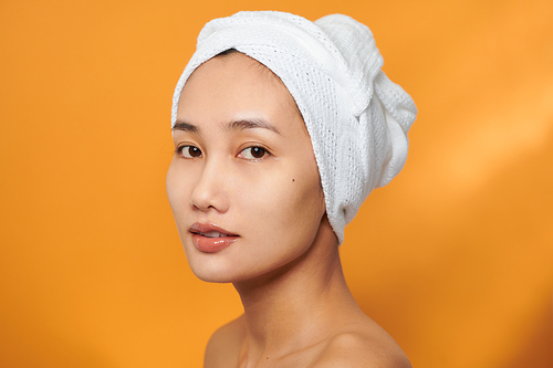 Closeup portrait of attractive smiling Asian woman blond wearing a towel on her head isolated on orange background, looking at camera