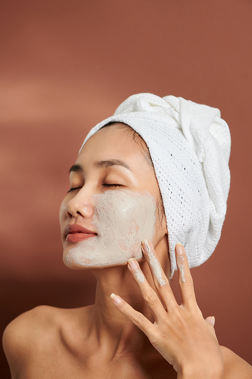 Focus on woman applying clay mask on her face.