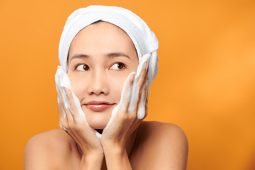 Laughing girl applying moisturizing cream on her face. Photo of young girl with flawless skin on orange background. Skin care and beauty concept
