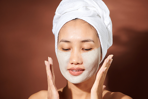 Young Asian woman applying clay mask on her face.